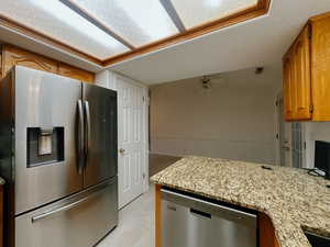 Kitchen with ceiling fan, light tile patterned floors, light stone counters, and appliances with stainless steel finishes