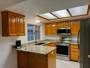 Kitchen with sink, light stone counters, kitchen peninsula, light tile patterned flooring, and appliances with stainless steel finishes