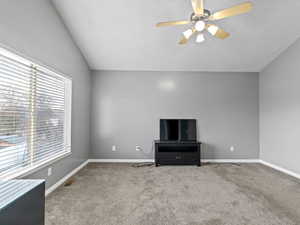 Unfurnished living room featuring ceiling fan, a healthy amount of sunlight, lofted ceiling, and light carpet