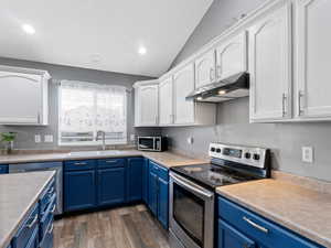 Kitchen with blue cabinetry, dark hardwood / wood-style flooring, vaulted ceiling, and appliances with stainless steel finishes