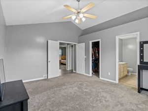 Unfurnished bedroom featuring connected bathroom, ceiling fan, light colored carpet, lofted ceiling, and a walk in closet