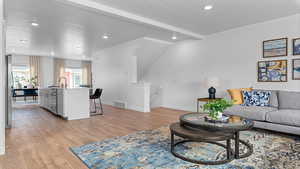 Living room with vaulted ceiling with beams, a textured ceiling, and light hardwood / wood-style floors