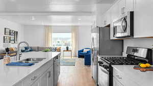 Kitchen featuring appliances with stainless steel finishes, a textured ceiling, sink, light hardwood / wood-style floors, and white cabinetry