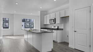 Kitchen featuring white cabinets, light wood-type flooring, an island with sink, and gas range