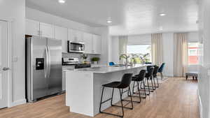 Kitchen with a kitchen island with sink, light wood-type flooring, appliances with stainless steel finishes, white cabinetry, and a breakfast bar area