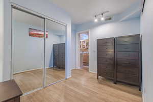 Unfurnished bedroom with ensuite bathroom, a closet, track lighting, and light hardwood / wood-style flooring