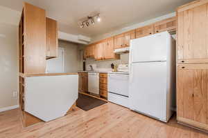 Kitchen featuring white appliances, sink, light brown cabinetry, and light hardwood / wood-style flooring