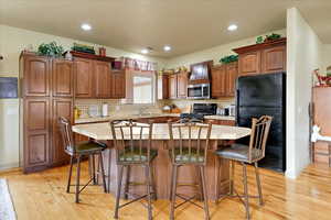 Kitchen with decorative backsplash, a kitchen island, black appliances, and light hardwood / wood-style floors