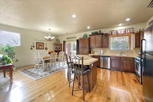 Kitchen with pendant lighting, light wood-type flooring, appliances with stainless steel finishes, a notable chandelier, and a kitchen island