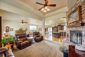 Living room featuring a raised ceiling, ceiling fan, a fireplace, and light wood-type flooring