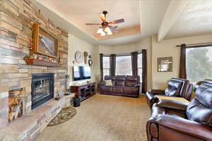 Carpeted living room featuring ceiling fan, a healthy amount of sunlight, a fireplace, and a tray ceiling