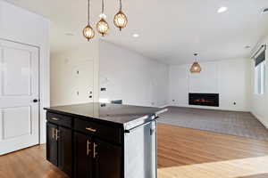 Kitchen with a center island, dark stone counters, light wood-type flooring, a fireplace, and decorative light fixtures