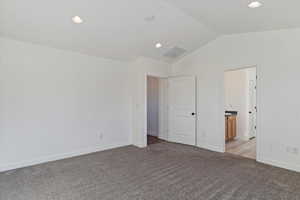 Unfurnished bedroom featuring light carpet, connected bathroom, and vaulted ceiling