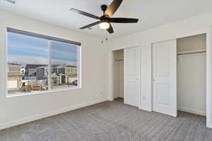 Unfurnished bedroom with multiple windows, ceiling fan, carpet, and two closets