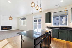 Kitchen featuring light wood-type flooring, sink, pendant lighting, dark stone countertops, and a kitchen island