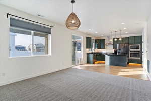 Kitchen featuring stainless steel appliances, a center island, wall chimney exhaust hood, and hanging light fixtures