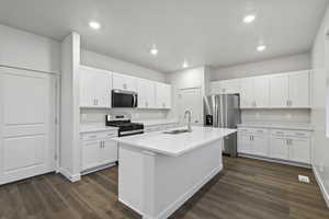 Kitchen featuring appliances with stainless steel finishes, white cabinetry, sink, dark wood-type flooring, and a center island with sink