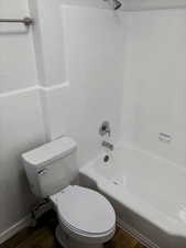 Bathroom with shower / tub combination, toilet, tile walls, and hardwood / wood-style flooring