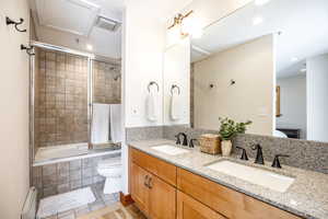 Full bathroom with vanity, shower / bath combination with glass door, tile patterned floors, toilet, and a baseboard radiator