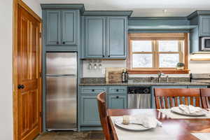 Kitchen featuring blue cabinetry, dark stone countertops, sink, and appliances with stainless steel finishes