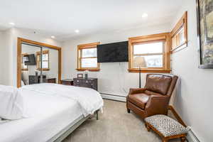 Carpeted bedroom with multiple windows, a closet, and baseboard heating