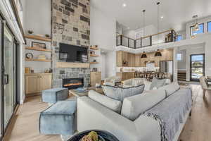 Living room featuring a towering ceiling, light hardwood / wood-style floors, and a stone fireplace