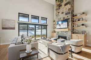 Living room with a high ceiling, light hardwood / wood-style floors, and a stone fireplace