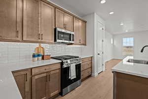 Kitchen with tasteful backsplash, appliances with stainless steel finishes, sink, and light hardwood / wood-style floors