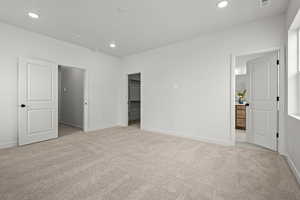 Unfurnished bedroom with connected bathroom, a spacious closet, and light colored carpet