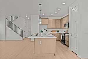 Kitchen with decorative light fixtures, an island with sink, sink, stainless steel appliances, and light hardwood / wood-style flooring