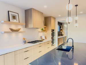 Kitchen with decorative backsplash, light brown cabinetry, stainless steel appliances, sink, and pendant lighting