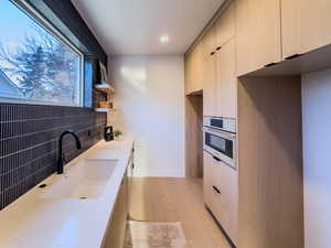 Kitchen with tasteful backsplash, stainless steel oven, sink, cream cabinets, and light hardwood / wood-style floors