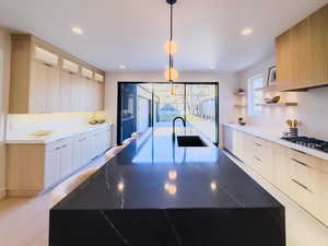 Kitchen with sink, white gas cooktop, hanging light fixtures, and light brown cabinetry