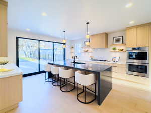 Kitchen with light brown cabinetry, stainless steel double oven, decorative light fixtures, and sink