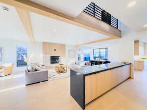 Kitchen with a large island, a large fireplace, light brown cabinets, beamed ceiling, and light hardwood / wood-style floors