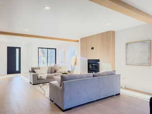 Living room with beamed ceiling, a large fireplace, and light hardwood / wood-style flooring