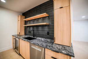 Kitchen featuring tasteful backsplash, stainless steel dishwasher, dark stone counters, sink, and light brown cabinets