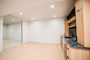 Bar featuring light brown cabinets, light carpet, dark stone counters, sink, and stainless steel dishwasher