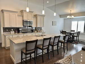 Kitchen featuring decorative light fixtures, sink, an island with sink, and dark wood-type flooring