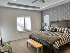 Carpeted bedroom with a raised ceiling, ceiling fan, and crown molding