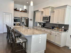 Kitchen featuring a center island with sink, sink, light stone countertops, appliances with stainless steel finishes, and dark hardwood / wood-style flooring