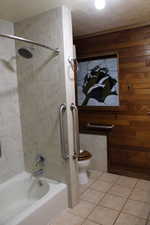 Bathroom featuring tile patterned floors, a textured ceiling, wooden walls, and tiled shower / bath