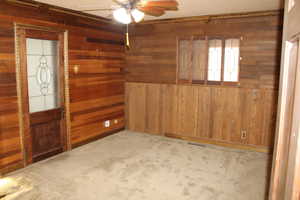 Spare room with wood walls, ceiling fan, and light carpet