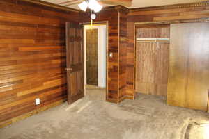 Unfurnished bedroom featuring carpet, ceiling fan, and wood walls