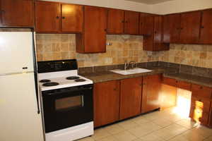 Kitchen featuring light tile patterned flooring, white appliances, backsplash, and sink