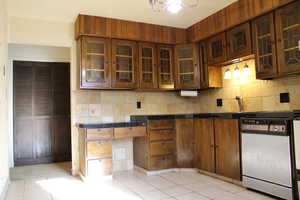 Kitchen featuring backsplash, dark brown cabinetry, white dishwasher, sink, and light tile patterned floors