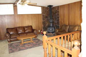 Living room featuring a wood stove, ceiling fan, and wood walls