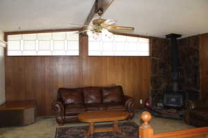 Living room with carpet, wood walls, a wood stove, ceiling fan, and a textured ceiling