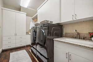 Laundry room with washing machine and dryer, cabinets, sink, and dark wood-type flooring