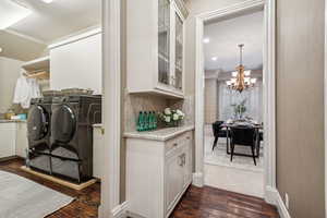 Laundry room with washing machine and clothes dryer, crown molding, dark hardwood / wood-style floors, and an inviting chandelier